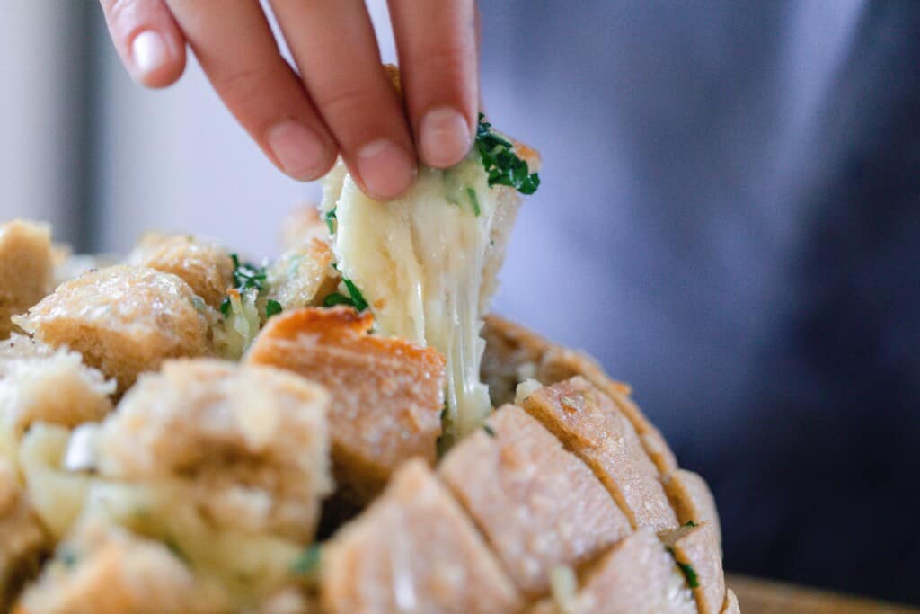 Someone grabbing a piece of sourdough pull apart bread with a perfect melted cheese pull