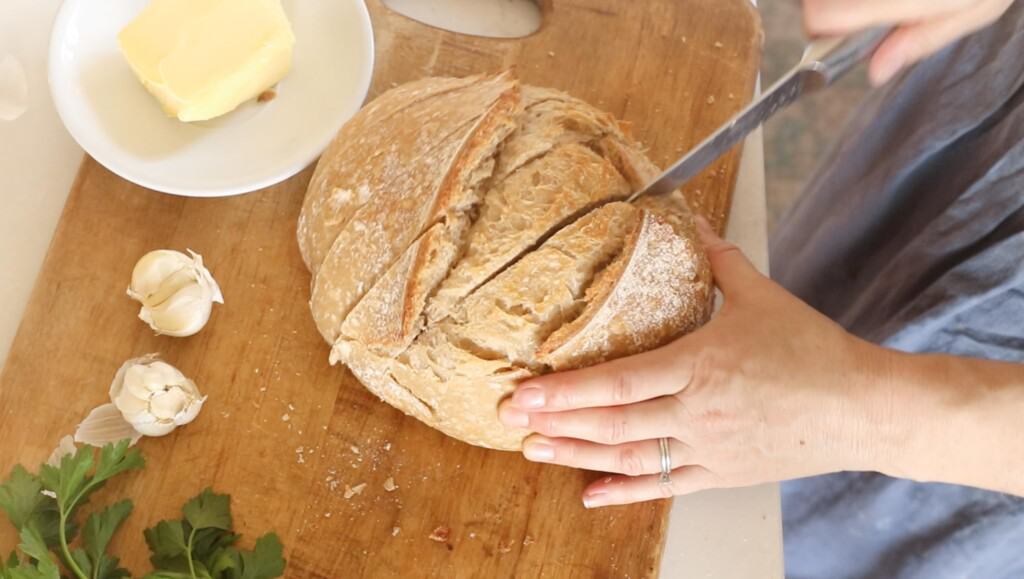 someone slicing a baked sourdough boule to create cuts for pull apart bread