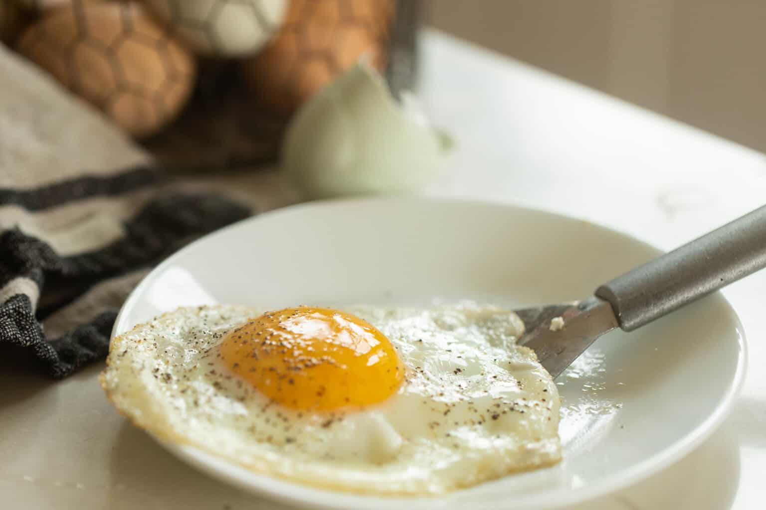 Sunny side up egg being set on a white plate with a silver spatula.