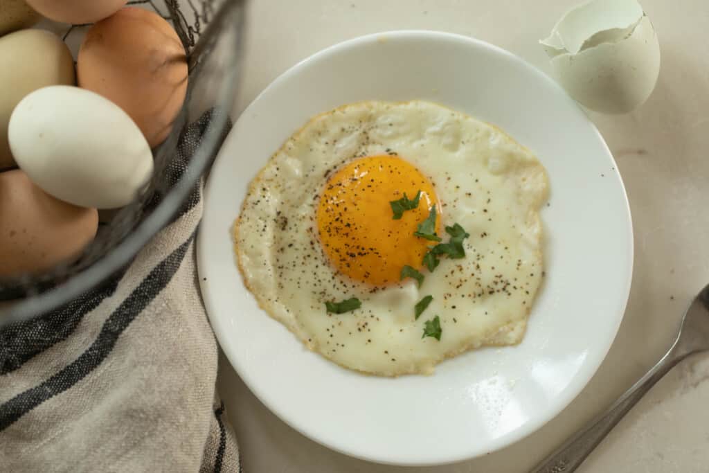 Sunny side up egg on white plate with herbs next to a tea towel