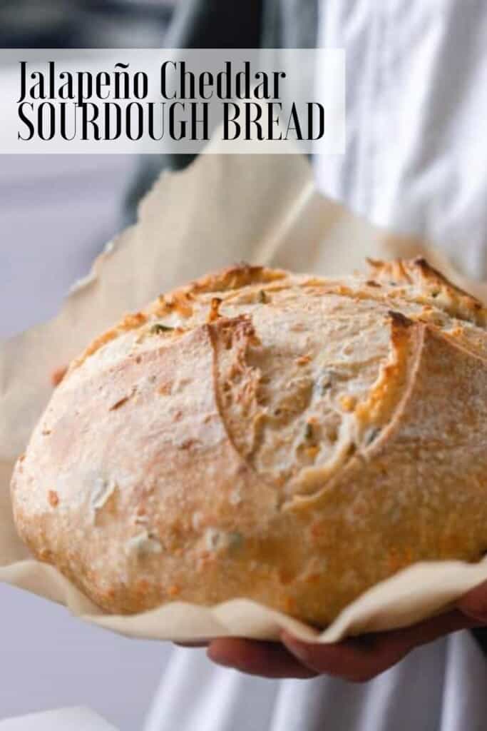 a girl holding a crust loaf of cheddar jalapeño sourdough bread on parchment paper