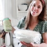 women holding. a blue mason jar of sauerkraut and a bowl of sourdough in her kitchen