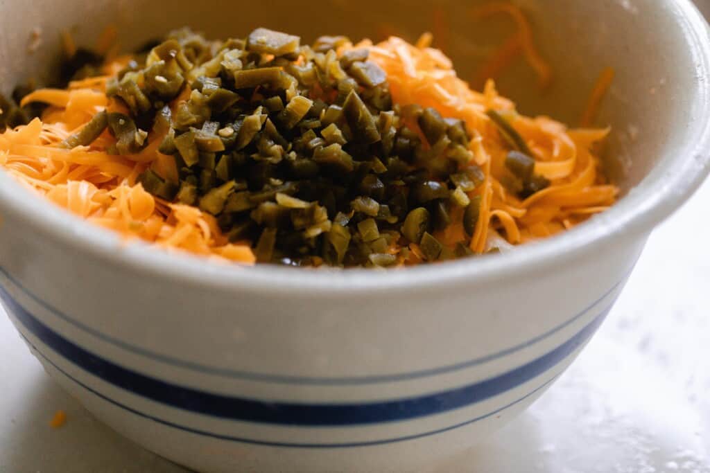 shredded cheese, chopped jalapeños and sourdough bread dough in a stoneware bowl