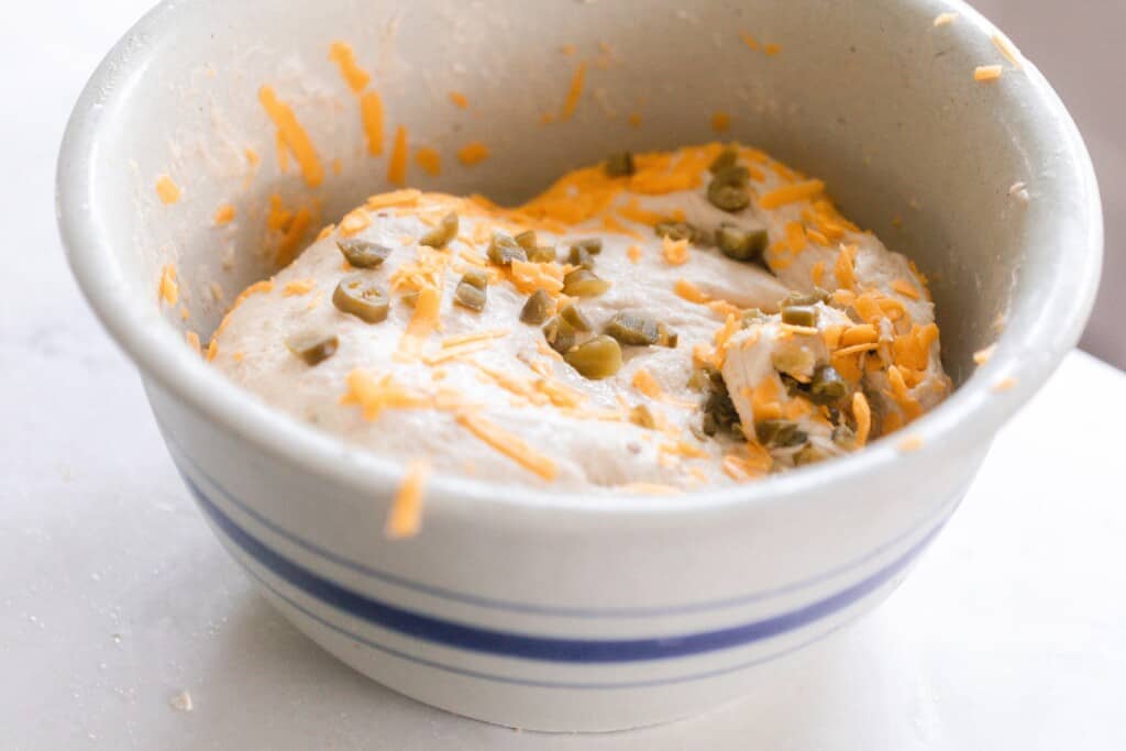 cheese and pickled jalapeños in bread dough in a white and blue ironstone bowl