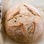 overhead photo of a crusty artisan loaf of cheddar jalapeño sourdough bread on parchment paper with a black and white stripped towel to the left