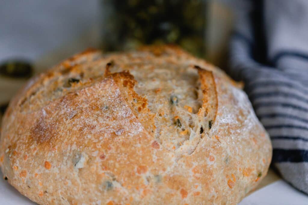 close up of a loaf of jalapeño cheddar sourdough bread on a black and white stripped towel