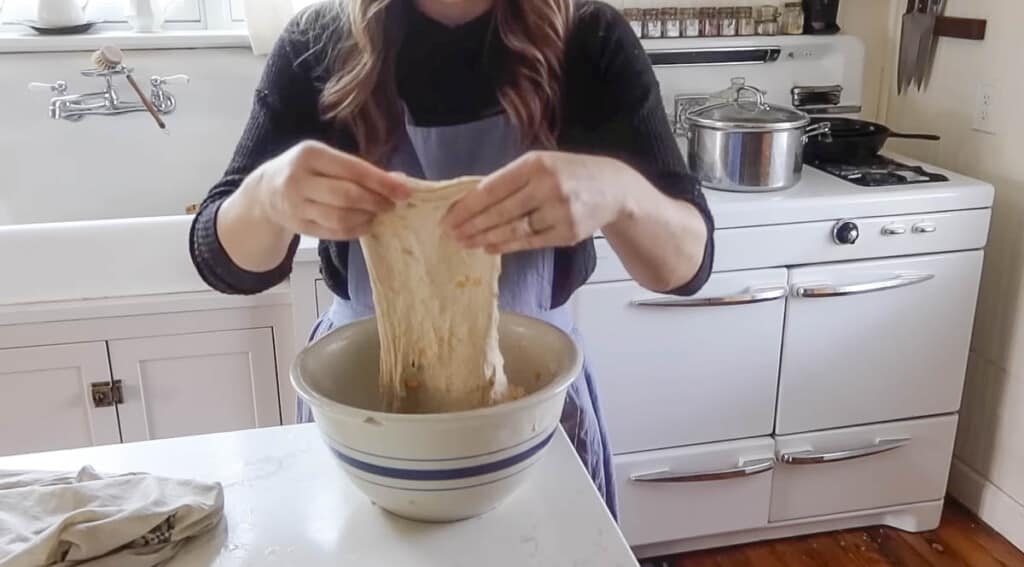 woman wearing a black shirt completing stretch and folds on a cheddar and jalapeño sourdough bread dough in a white kitchen