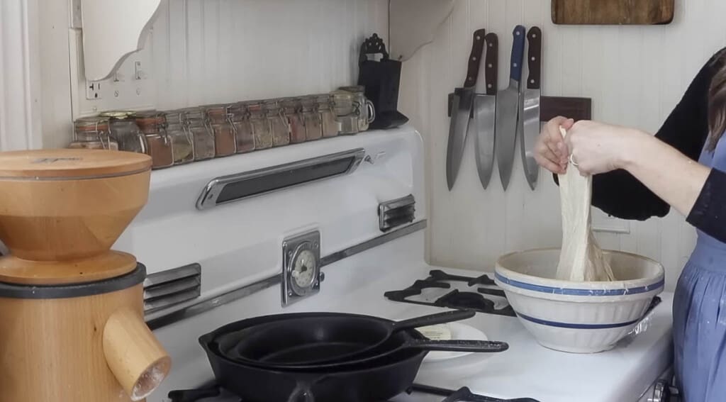 woman completing stretch and folds to dough in a bowl on a antique stove