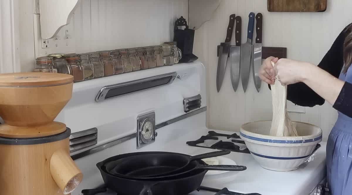 woman completing stretch and folds to dough in a bowl on a antique stove