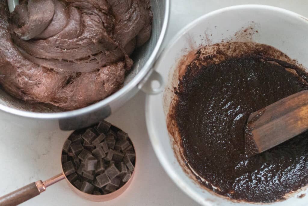 a bowl of chocolate dough, a bowl of sugar and chocolate filling, and a copper measuring cup full of chocolate chunks