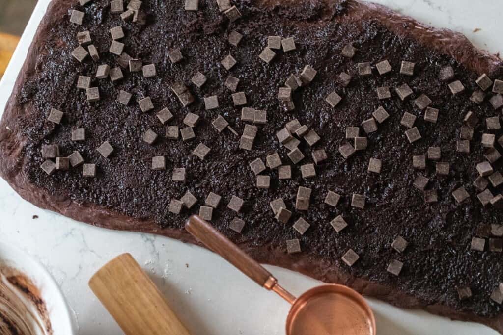 chocolate dough rolled into a rectangle with a chocolate sugar mixture spread on the dough and chocolate chips sprinkled on top