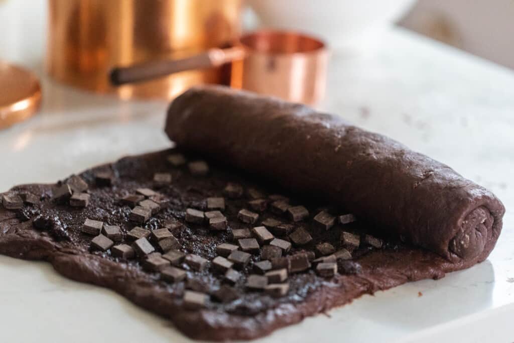 rolling up a sourdough double chocolate sweet roll on a white countertop