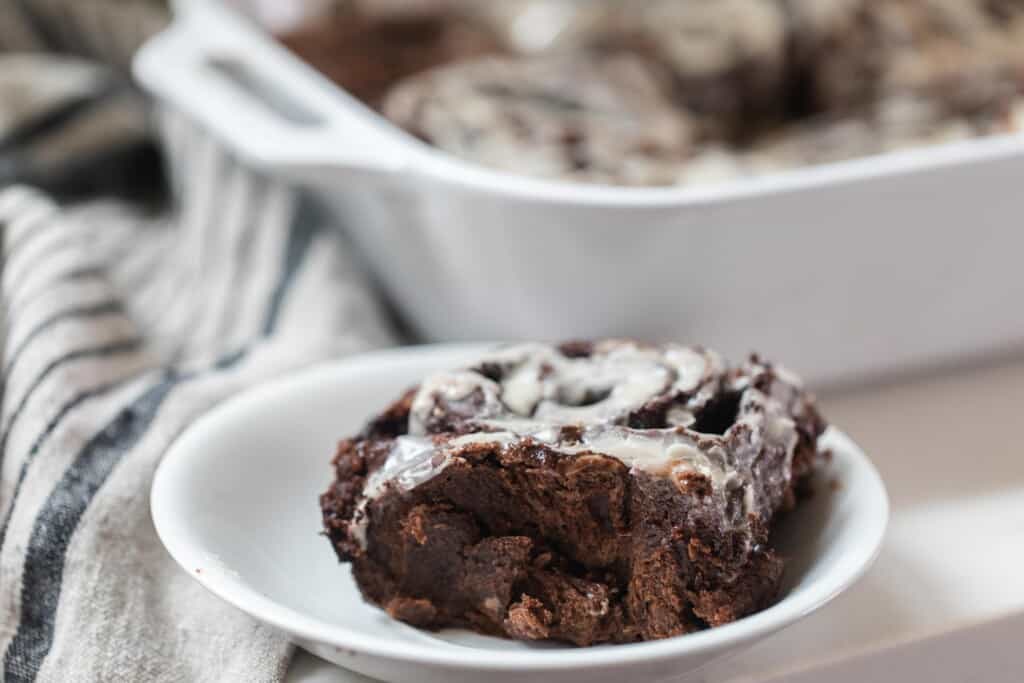 chocolate sourdough roll on a white plate with a white baking dish with more rolls in the background