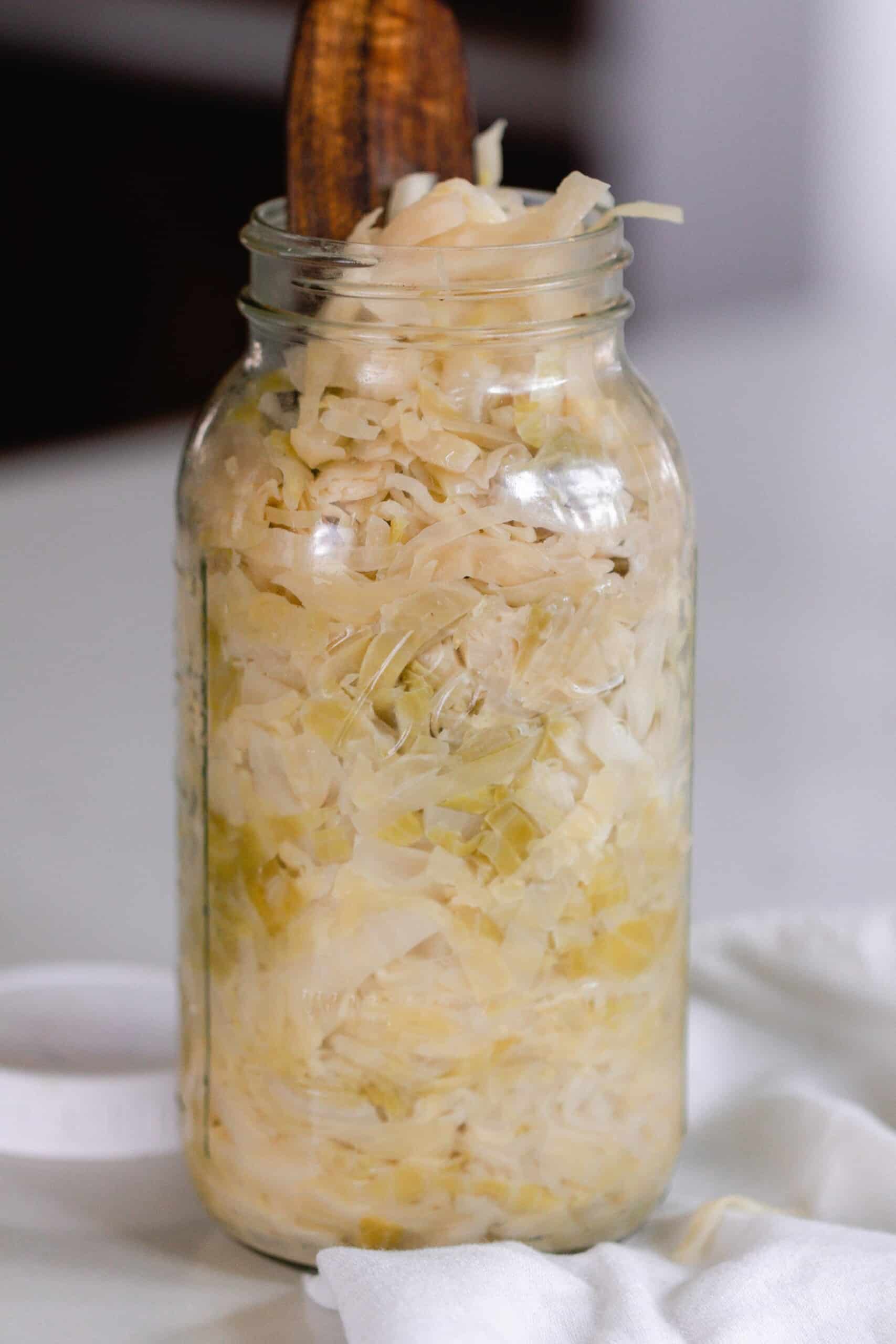 sauerkraut in a glas mason jar with a wooden spatula sticking out
