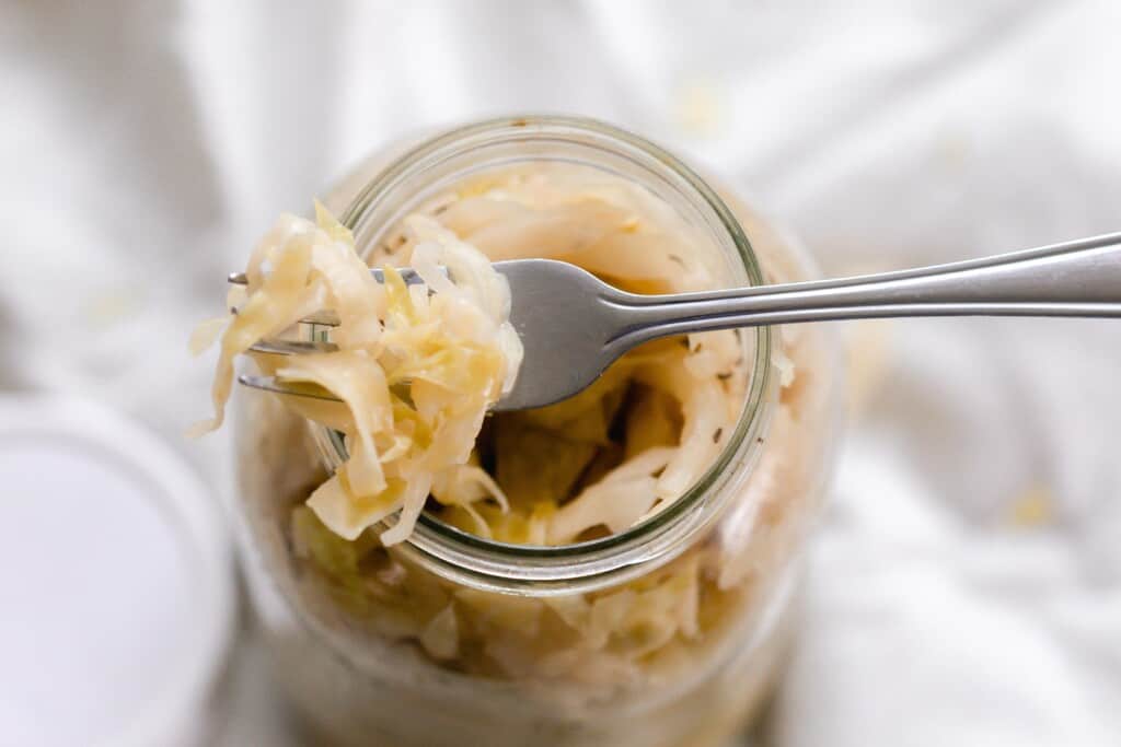 overheat photo of a fork with sauerkraut sitting on top of a jar of sauerkraut