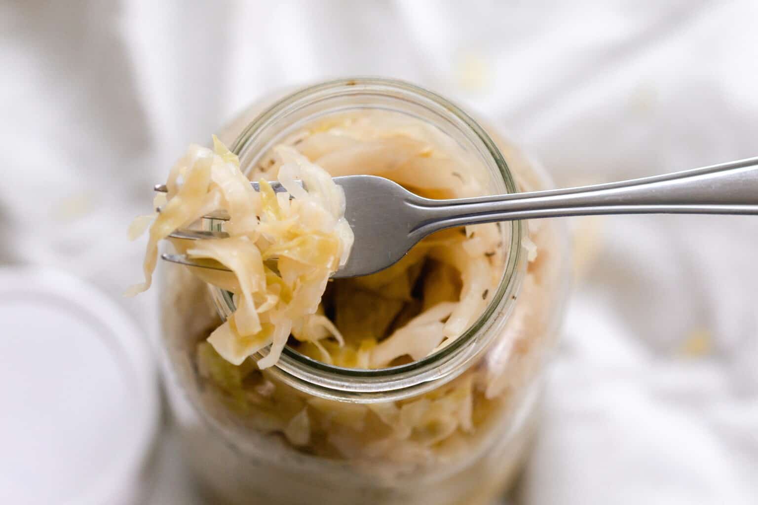 A fork scooping fermented sauerkraut out of a mason jar.