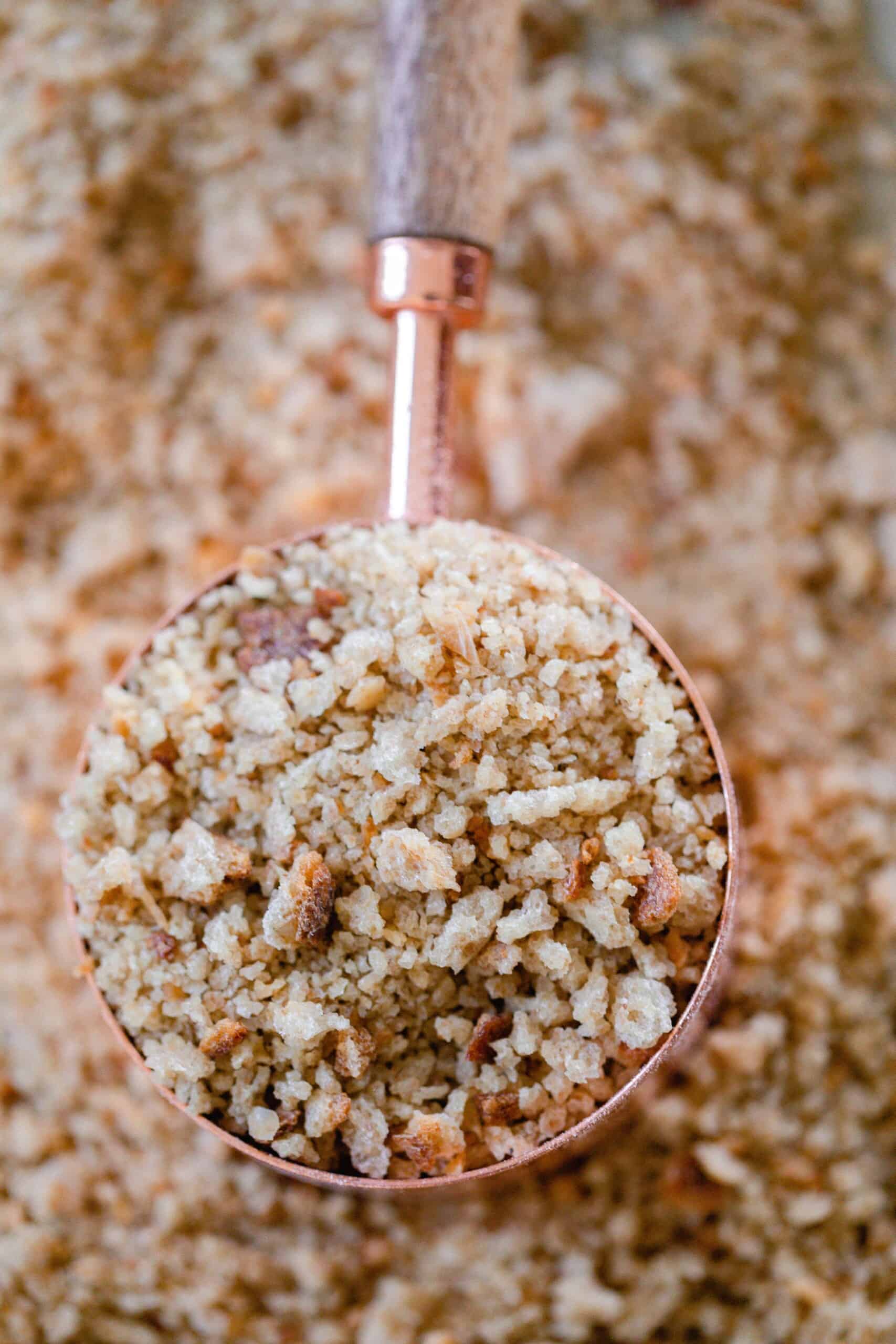 a copper and wood dry measuring cup full of sourdough bread crumbs on a sheet of more breadcrumbs