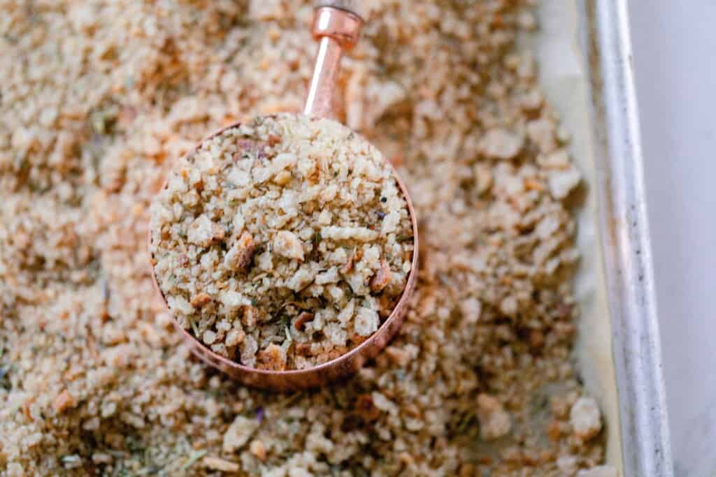 a copper measuring cup full of breadcrumbs on a baking sheet of bread crumbs