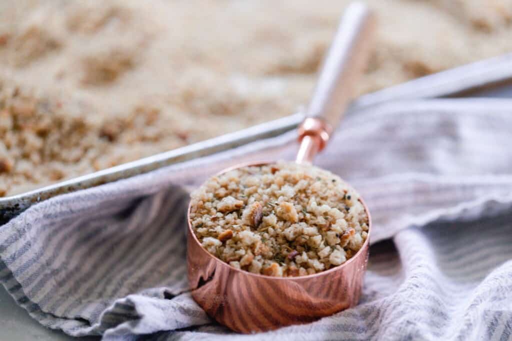 sourdough bread crumbs in a copper measuring cup on a gray and white stripped towel