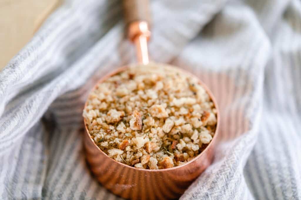 sourdough bread crumbs in a copped measuring cup on a white and gray stripped towel