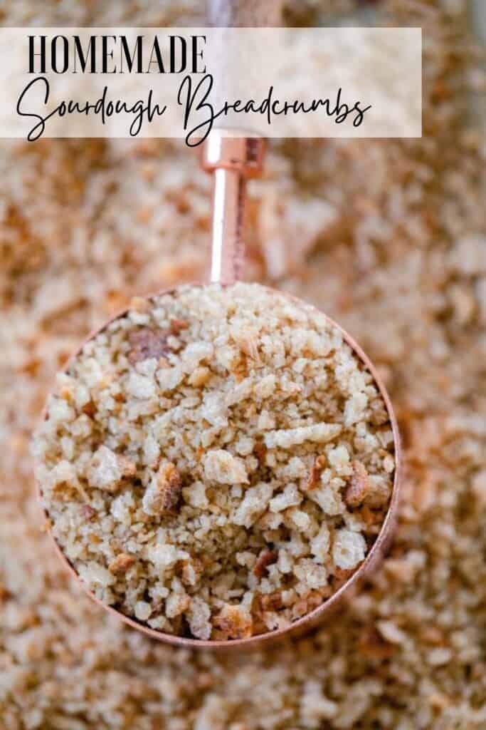 a copper and wood dry measuring cup full of sourdough bread crumbs on a sheet of more breadcrumbs