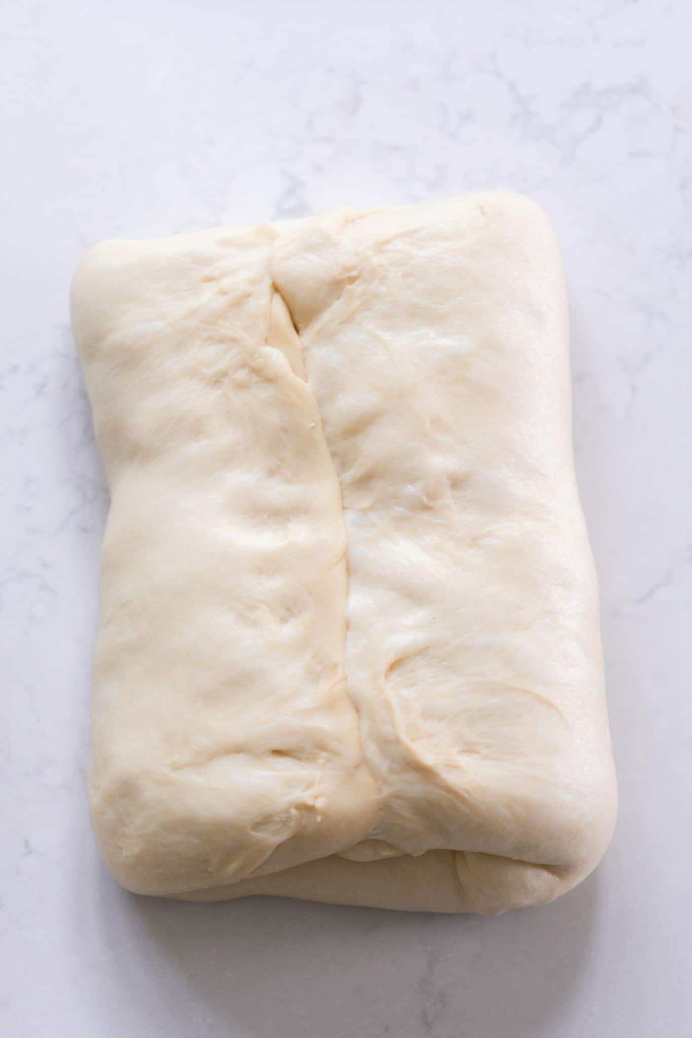 Shaping sourdough panettone by folding in two sides on a white counter top background