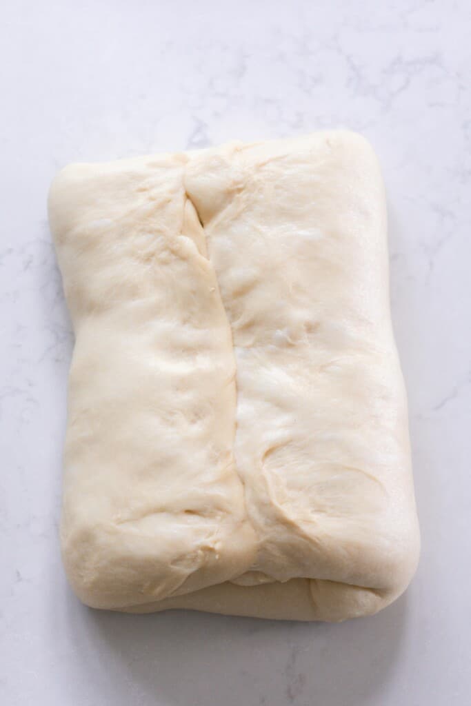 Shaping sourdough panettone by folding in two sides on a white counter top background