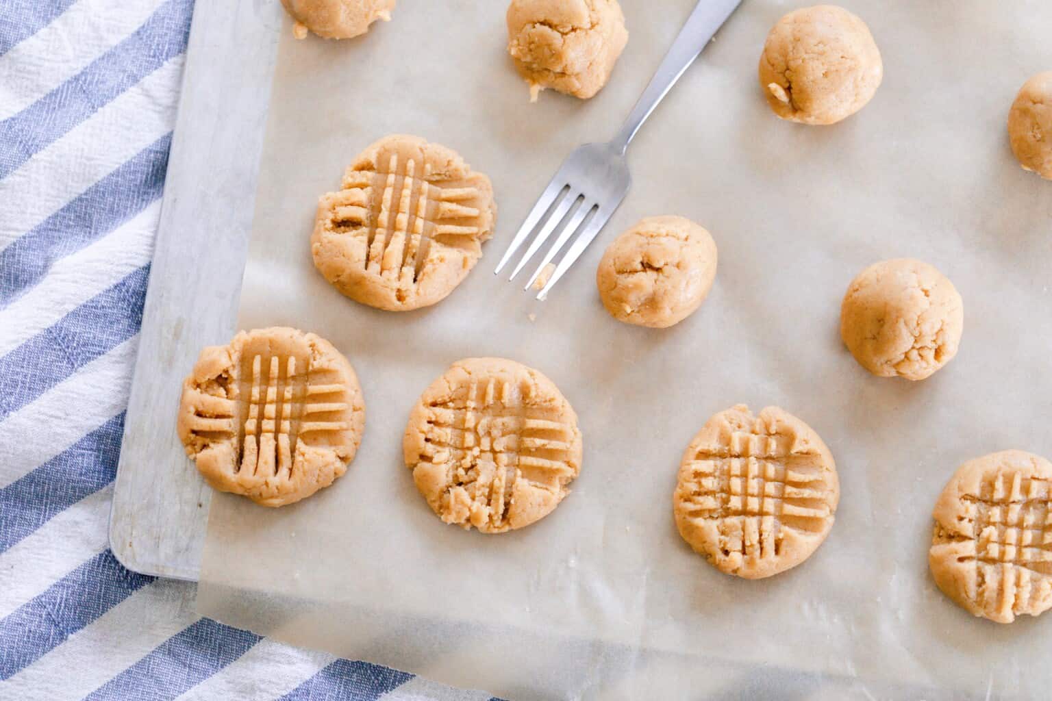 sourdough peanut butter cookies rolled into balls and some are pressed with a fork on top on parchment paper