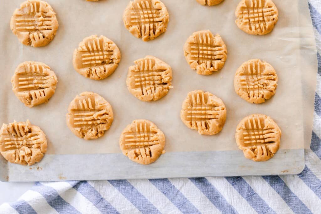 overhead photo of sourdough peanut butter cooke dough pressed on parchment paper on a white and blue stripped towel