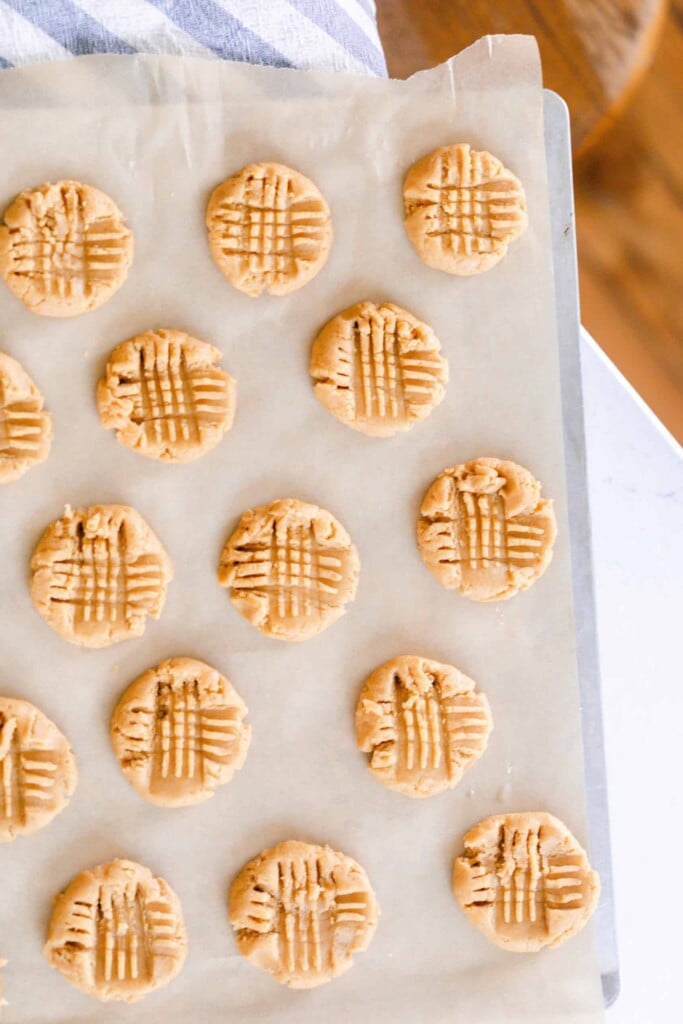 sourdough peanut butter cookies on parchment paper on a white countertop with a blue and white stripped towel in the back