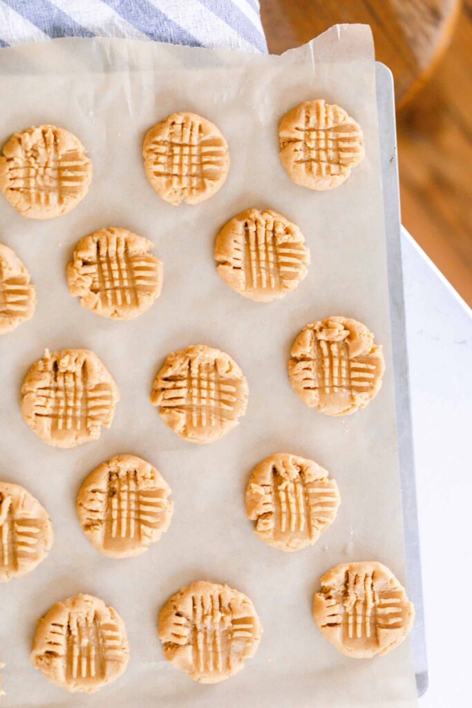 sourdough peanut butter cookies on parchment paper on a white countertop with a blue and white stripped towel in the back