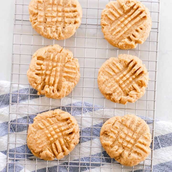 six sourdough peanut butter cookies on a wire rack on a white countertop with a blue and white tea towel