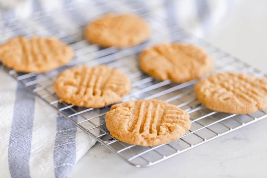 six sourdough peanut butter cookies on a wire rack on a blue and white stripped towel and counter