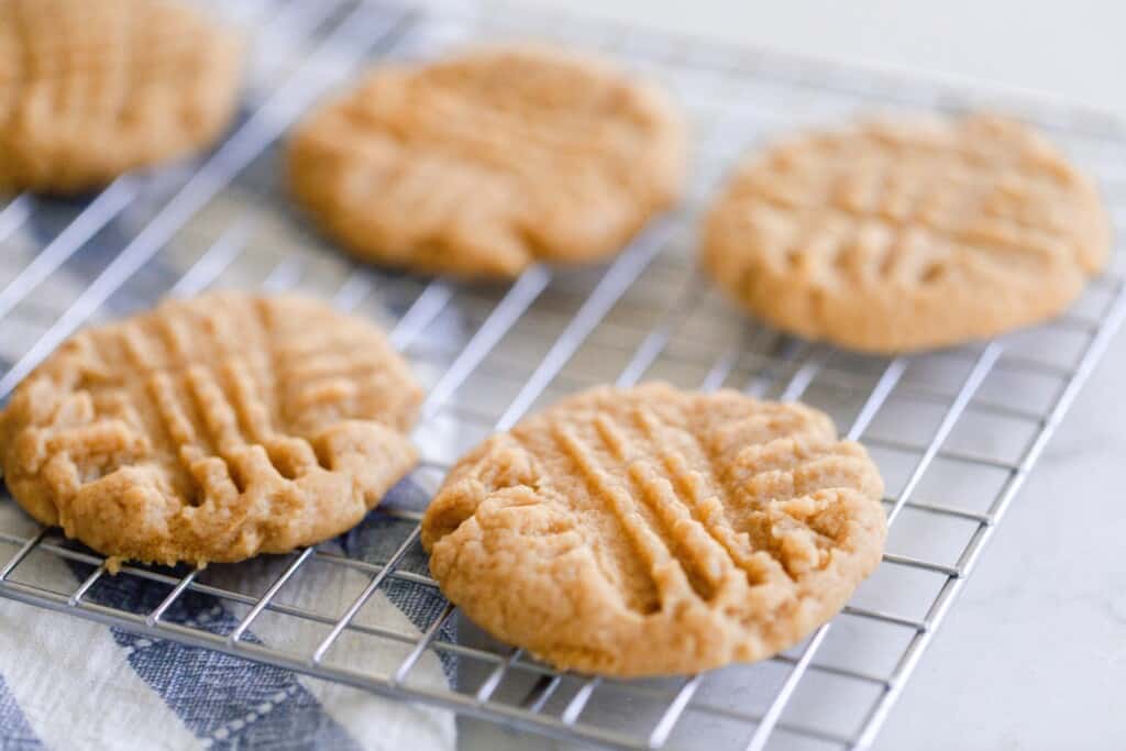four peanut butter cookies on a cooling wrack on top of a blue and white stripped towel
