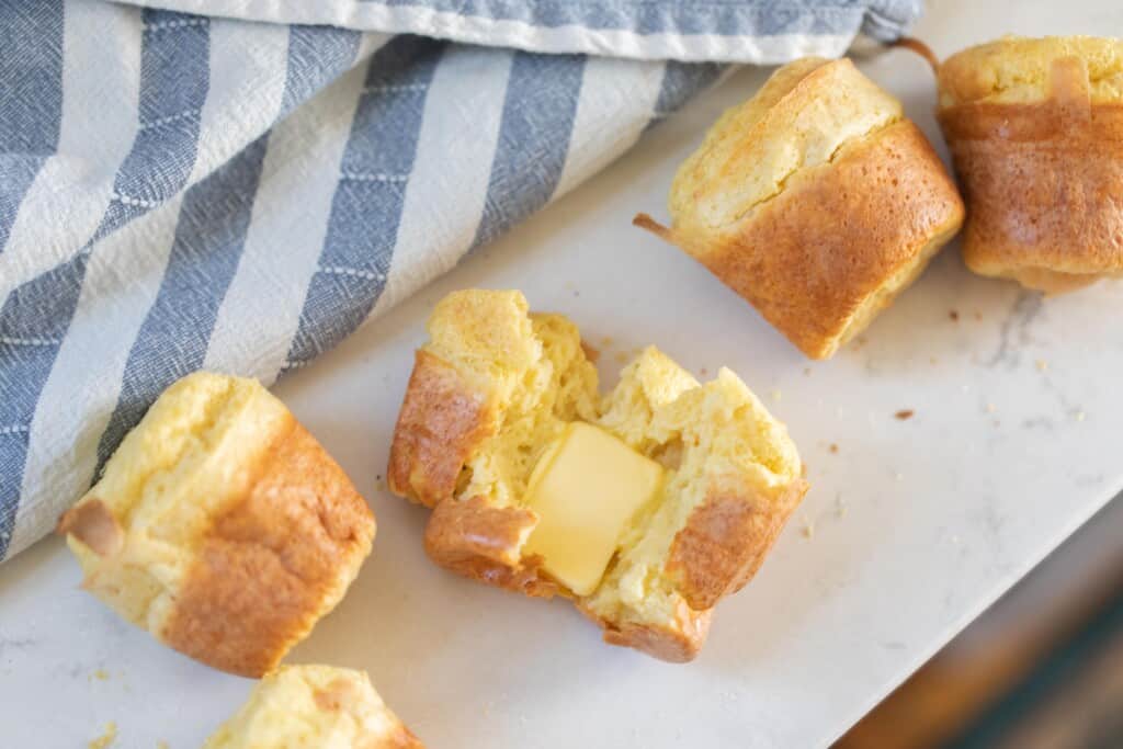 sourdough popover with butter on a white countertop next to a blue and white striped tea towel