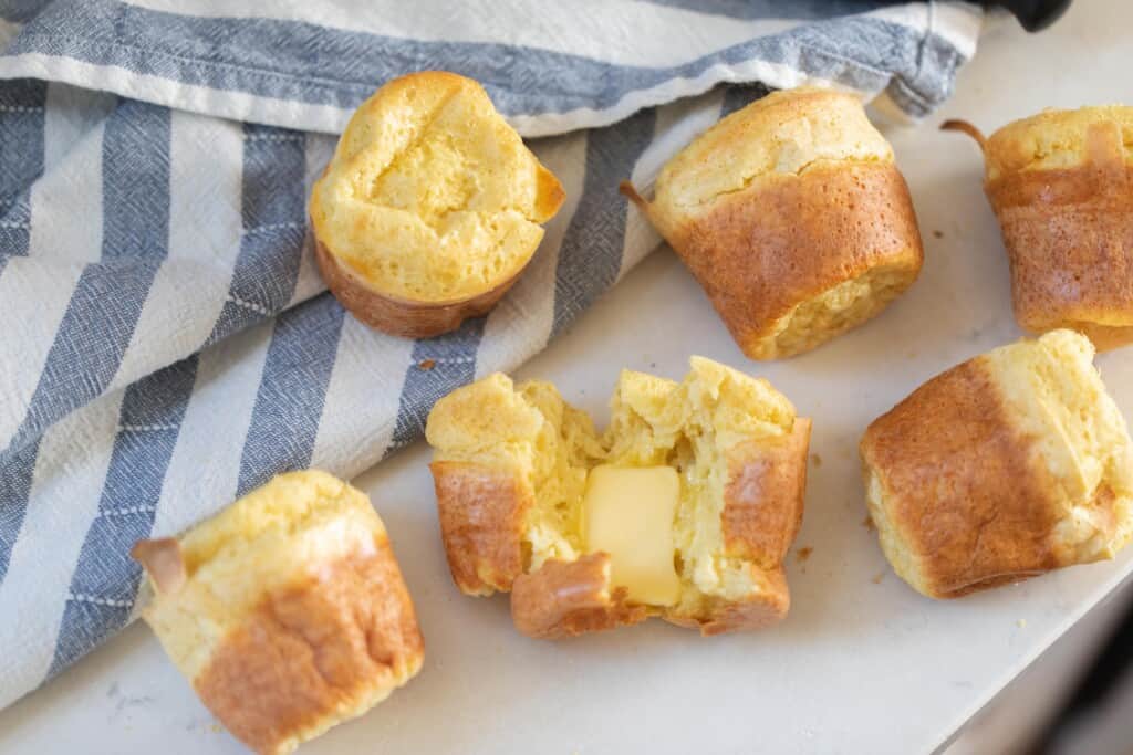 six sourdough popovers on a white countertop next to a blue and white striped tea towel