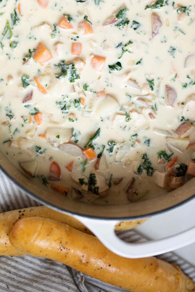 Chicken kale soup in a white dutch oven with bread sticks on the side of the dutch oven