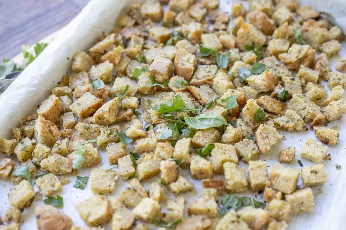 Parchment lined sheet pan with gluten free croutons topped with fresh herbs.