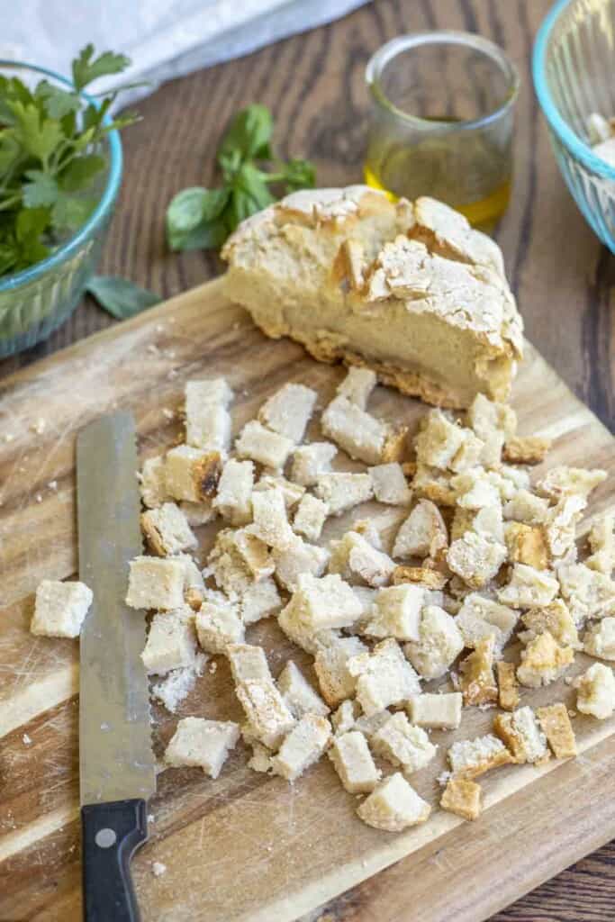 loaf of gluten free bread diced up on a cutting board with jars and fresh herbs around the cutting board