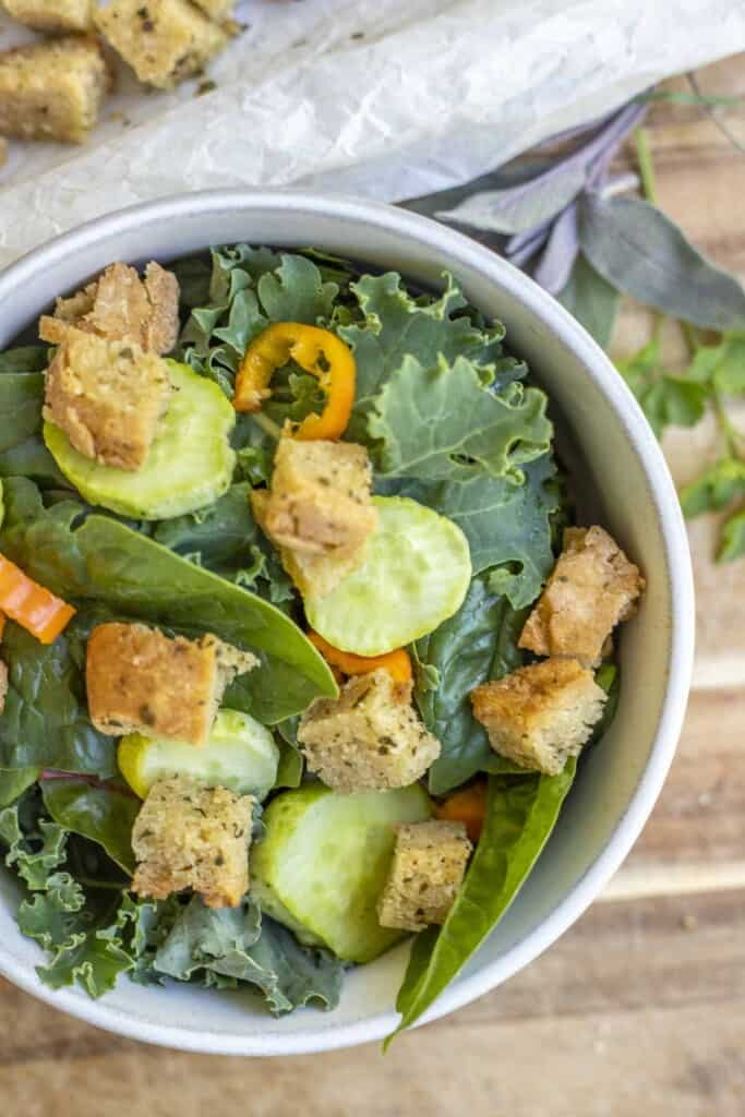 overhead photo of a kale salad topped with cucumbers, sliced peppers, and gluten free croutons