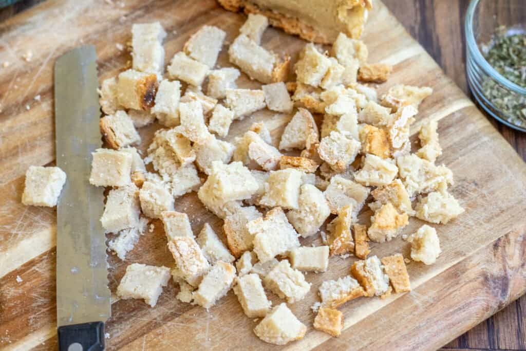 Cubed gluten free bread on a cutting board with a knife.