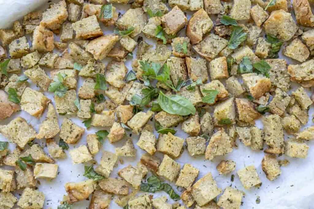 gluten free croutons topped with fresh herbs on a parchment lined baking sheet