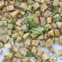 gluten free croutons topped with fresh herbs on a parchment lined baking sheet