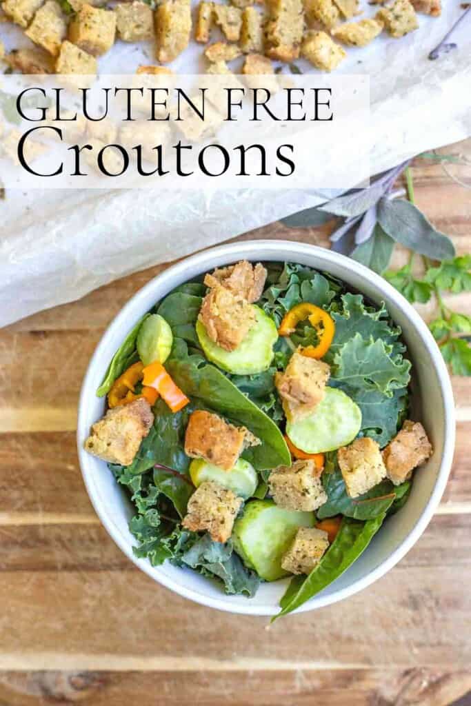 overhead photo of a salad topped with sliced cucumbers and peppers in a bowl with a tray of croutons in the background