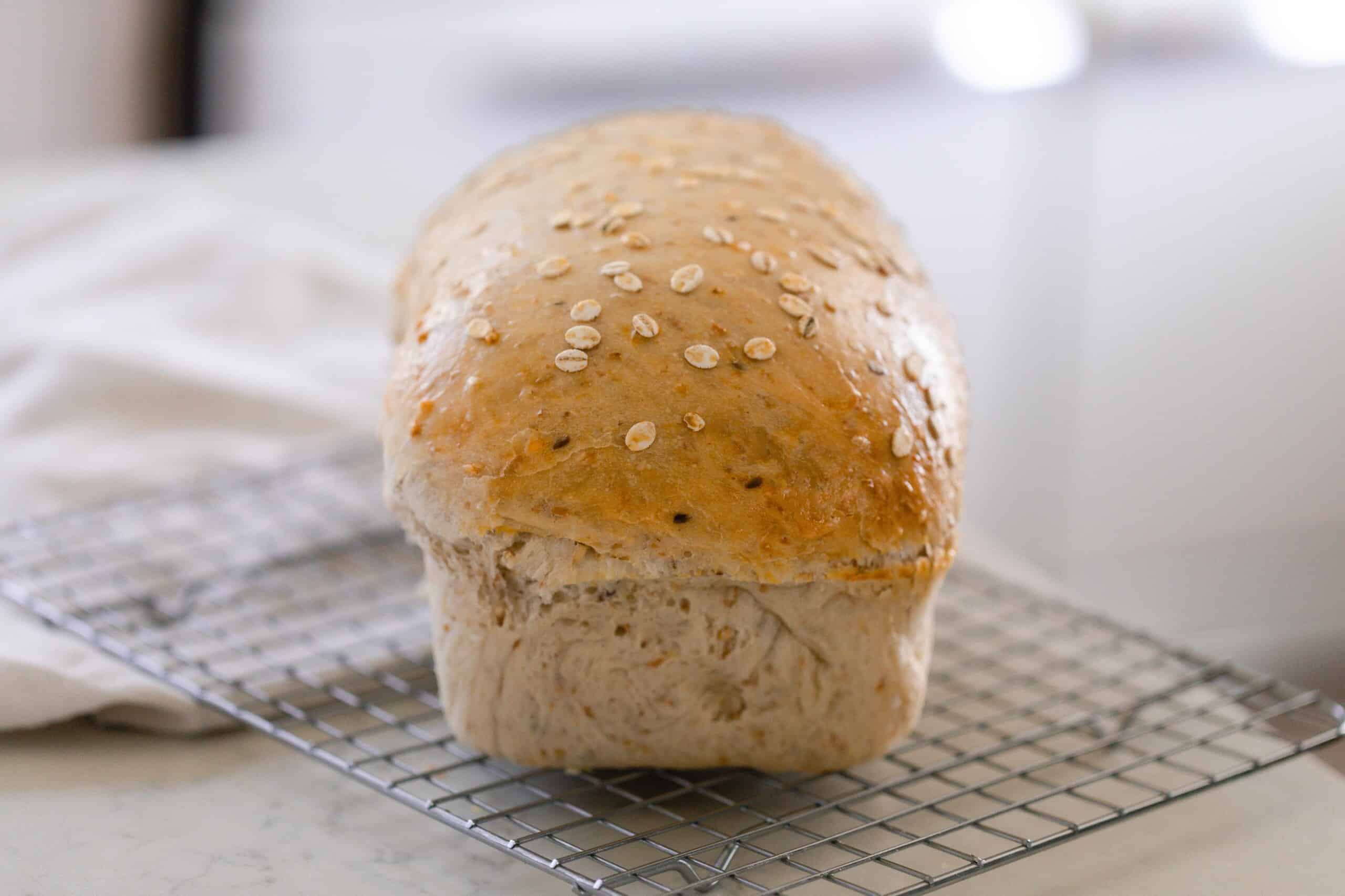 loaf of sourdough multigrain bread on a wire rack on a white countertop with a white towel in the background