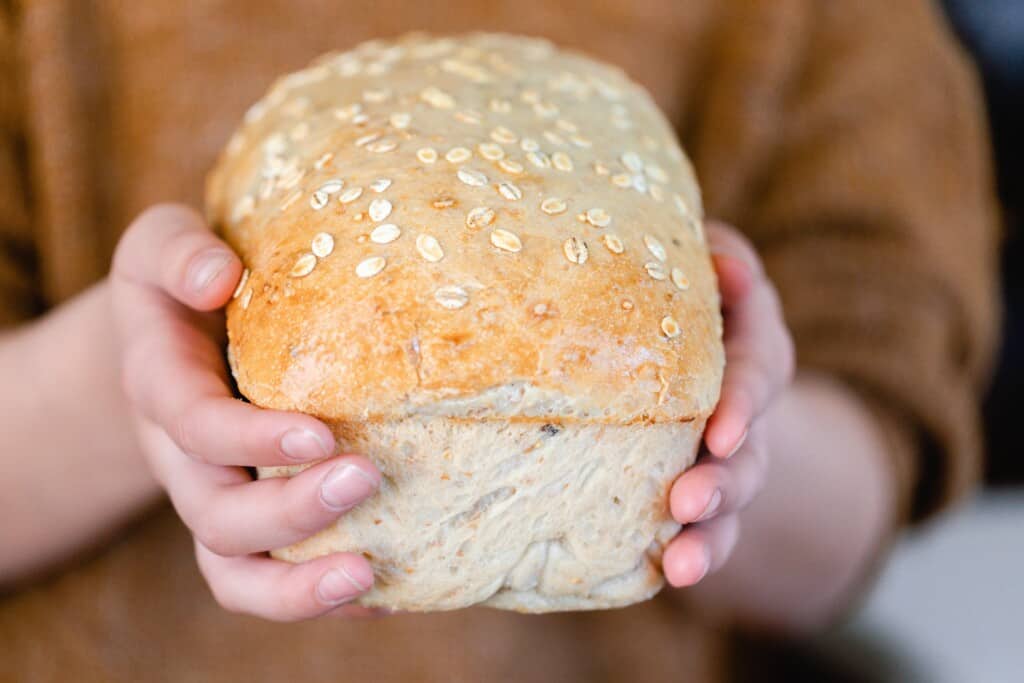 hands holding a loaf of soft multigrain sourdough bread topped with oats
