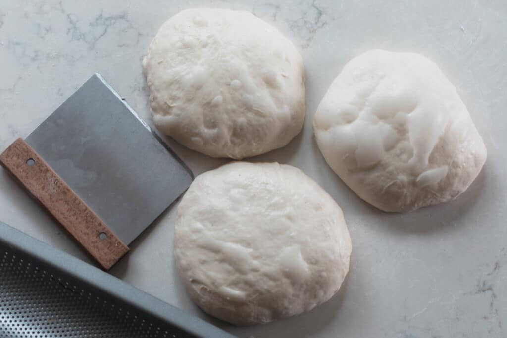 Three balls of dough sitting on a white countertop with a bread cutter