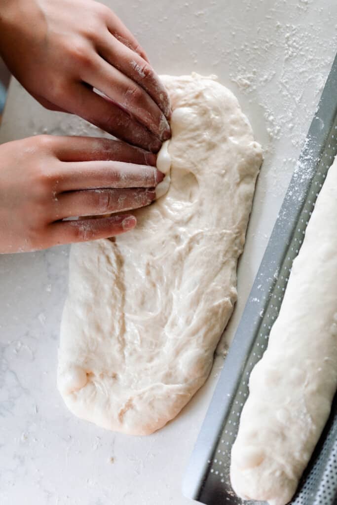 Two hands shaping sourdough baguette dough