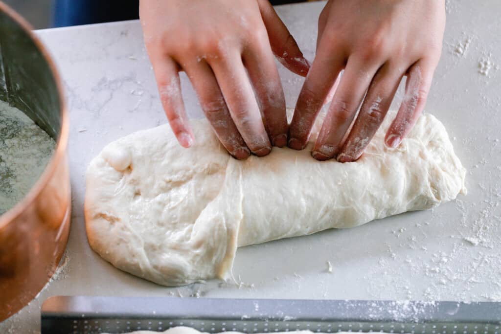 two hands shaping sourdough baguette dough by folding it over