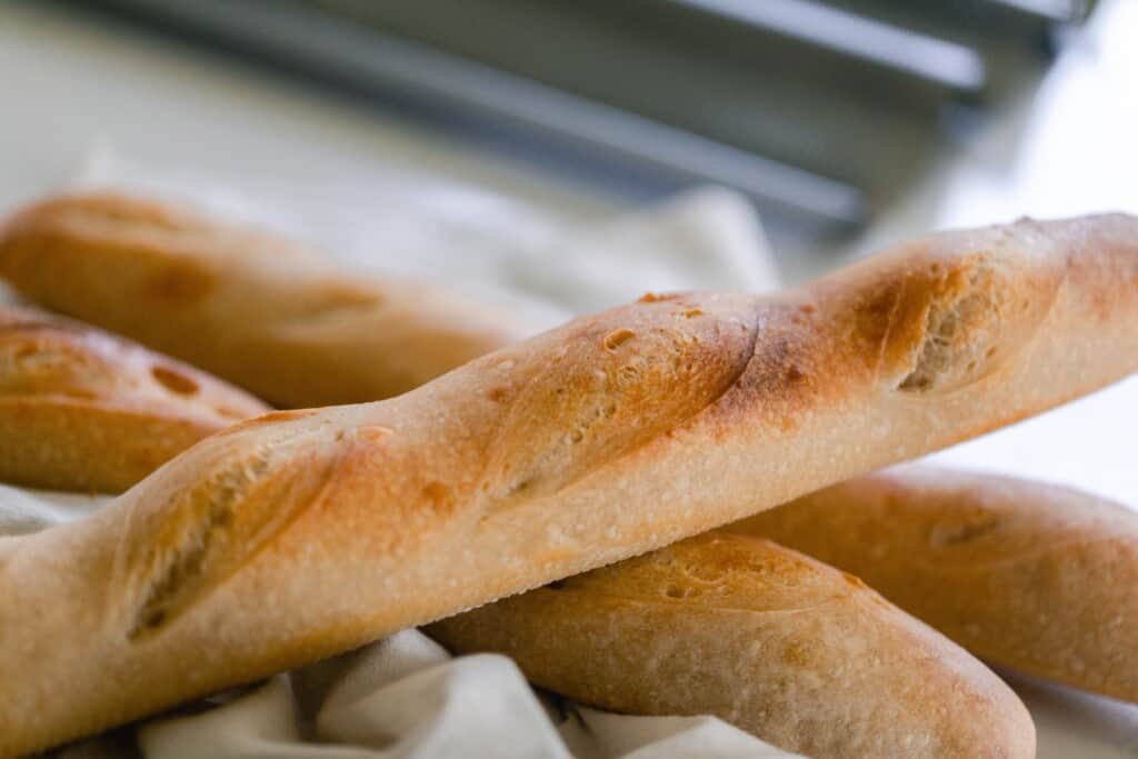 Sourdough baguette stacked on two other baguettes on a white tea towel